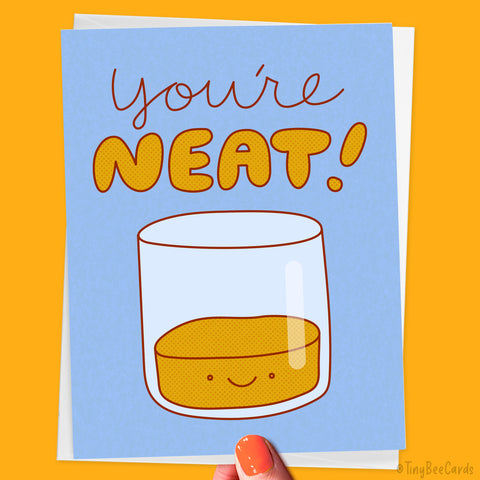 Greeting card with a glass of alcohol and 'You're NEAT!' text on a blue background, held against an orange background.