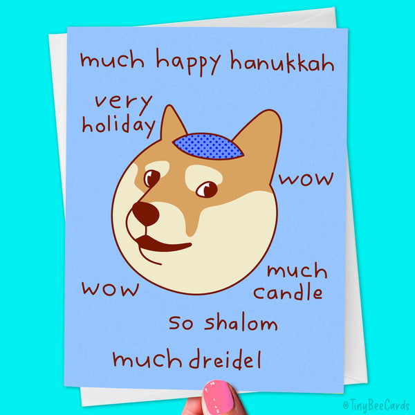 A Hanukkah card featuring a hand drawn artwork of a shiba inu doge meme dog wearing a yarmulke, with hand drawn text surrounding that says "much happy hanukkah, very holiday, wow, much candle, so shalom, much dreidel"