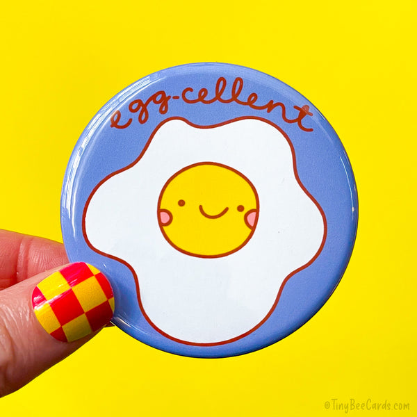 Button badge with a hand drawn smiley face egg design and 'egg-cellent' text 