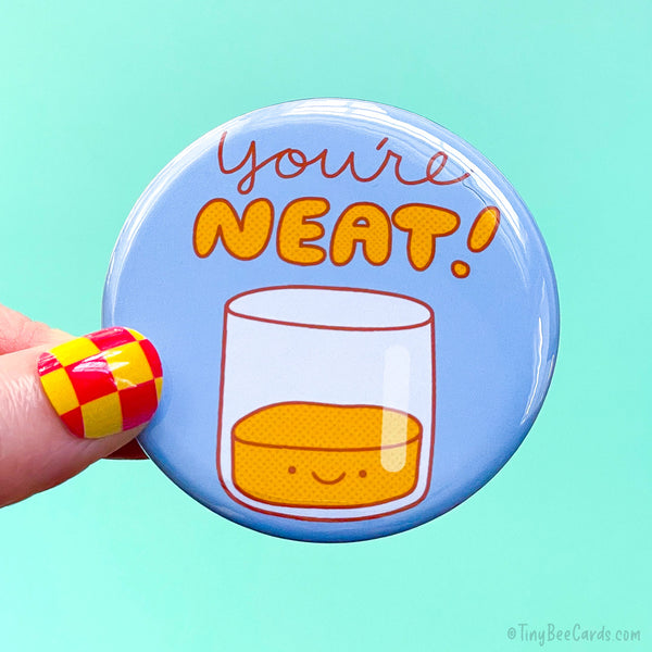 Button badge with a hand drawn neat alcohol drink with a happy face, and the text 'You're NEAT!' on a light blue background.