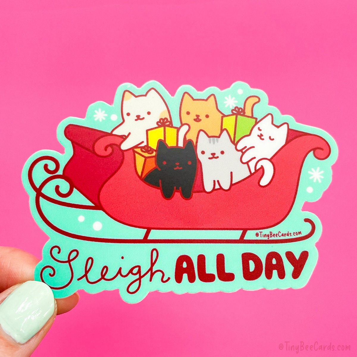 A fun and festive vinyl sticker featuring a cute cat squad with a black cat, a calico, an orange cat, a white cat, and a grey striped cat, all in a Christmas sleigh with plenty of presents. The pun text below says "Sleigh all day."