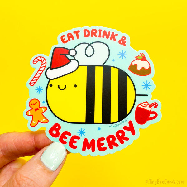 Cute Christmas and holiday vinyl sticker featuring a bumblebee surrounded by yummy holiday foods (figgy pudding, candy cane, gingerbread man, and hot cocoa) with the pun text "Eat Drink and bee Merry" 